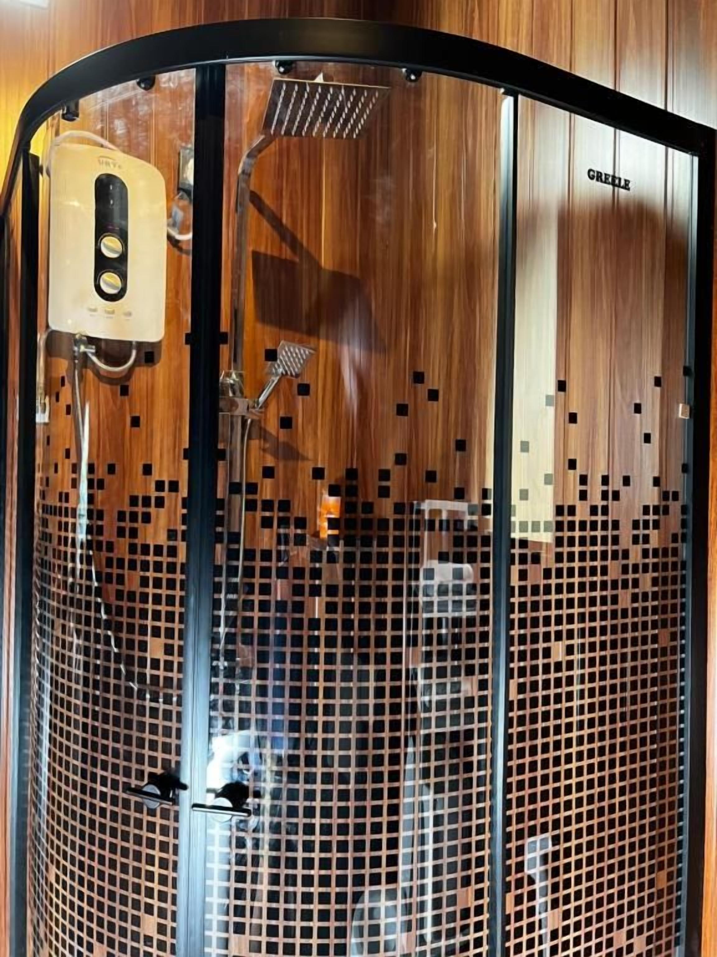 A shower enclosure with a glass door, a handheld showerhead, and a control panel.