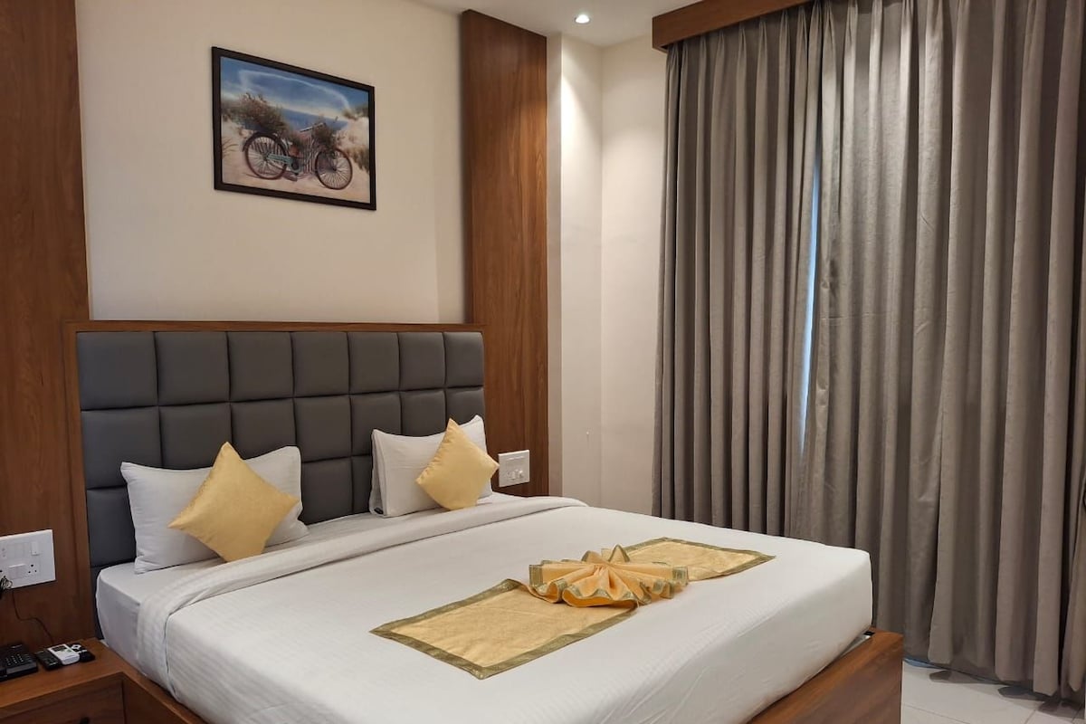 Habitación de hotel con una cama grande, cabecero, mesita de noche y una ventana con cortinas.