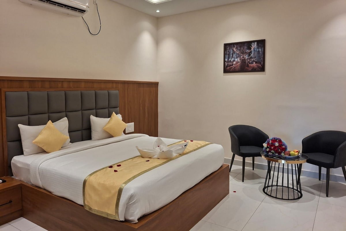 A hotel room with a large bed, a bedside table, a chair, a small round table with a vase of flowers, and a painting on the wall.