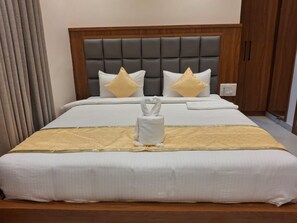 A hotel room with a large bed, a wooden headboard, and a white towel centerpiece. - SRS Elegance (Bengaluru)