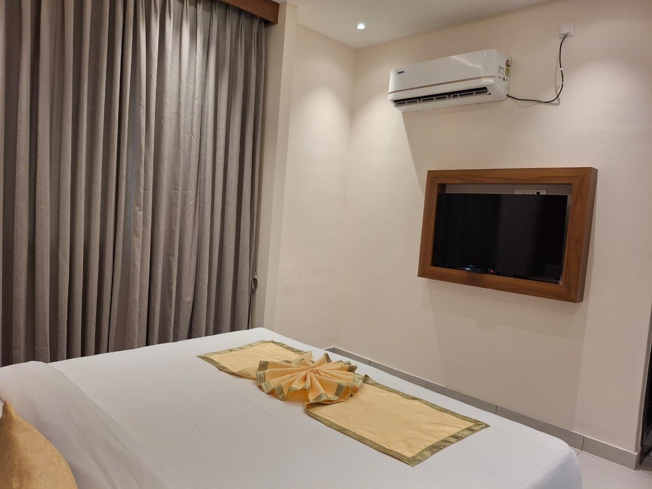 A hotel room with a bed, an air conditioning unit, a television, and a window with curtains.