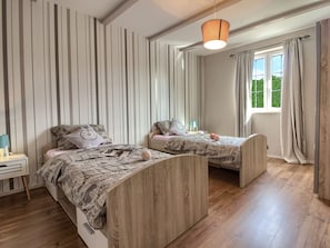 A bedroom with two single beds, a nightstand with a lamp, a window with curtains, and a hanging light fixture. - Villa Nikolina 2km Beach (Liznjan)
