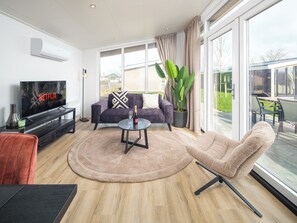 Een moderne woonkamer met een flatscreen televisie, een bank, een salontafel en een groot raam met uitzicht op de omgeving.