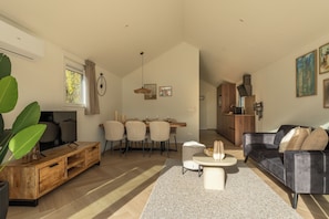 A modern living room with a TV, wooden furniture, a dining area with chairs, and a kitchen in the background. - Go out and discover the oyster culture in Yerseke together! (Yerseke)