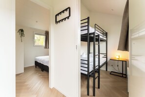 Un dormitorio con literas, una mesita de noche con lámpara, una ventana con cortinas y una planta en maceta.