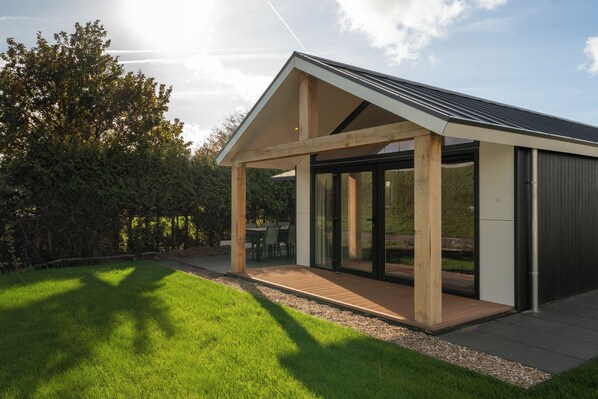 Eine moderne Außenarchitektur mit geneigtem Dach, großen Glasfenstern und einer Holzterrasse.