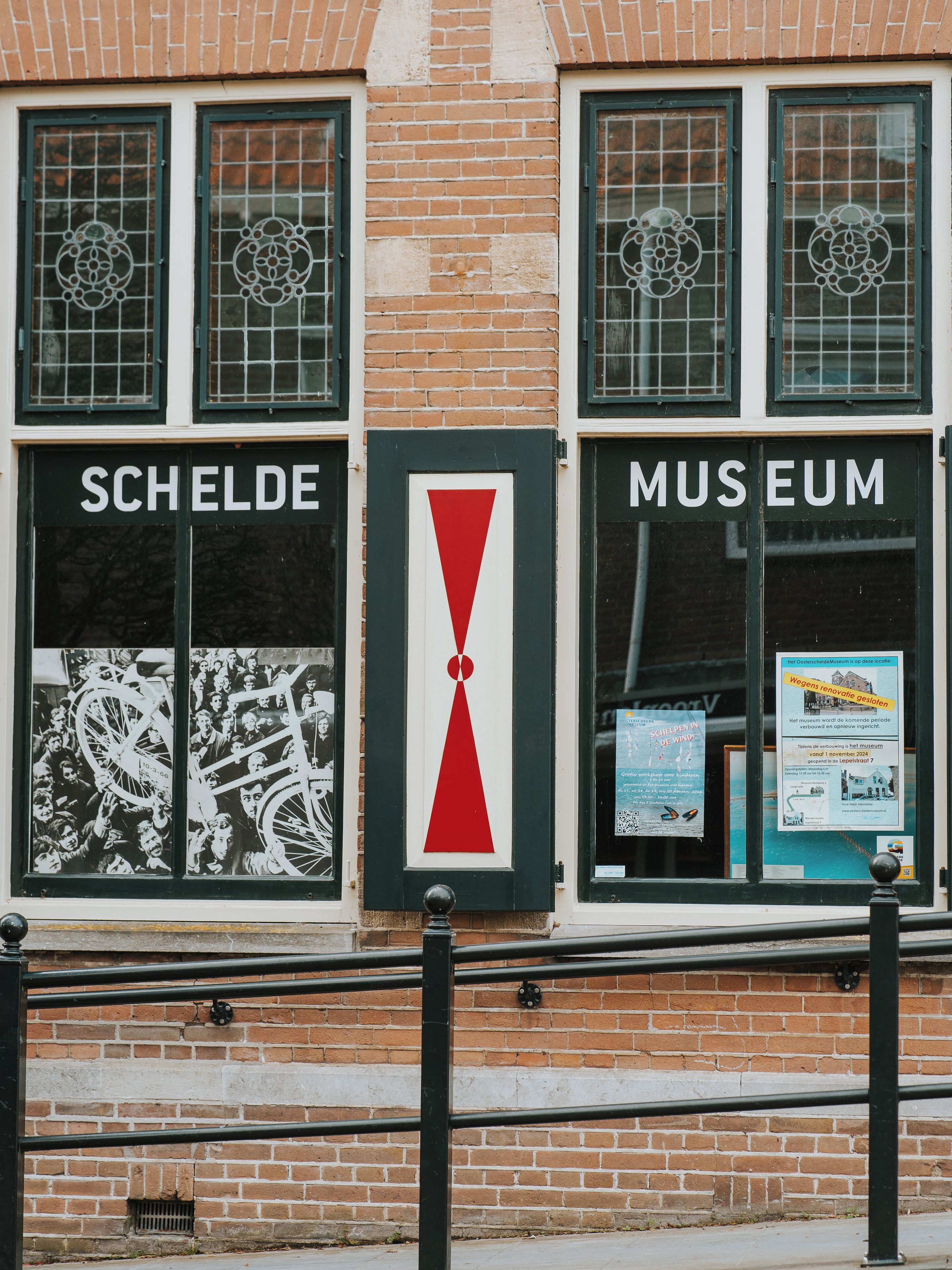 Een gevel met ramen waarop 'SCHELDE' en 'MUSEUM' staat, een rood en wit bord en een bakstenen muur.
