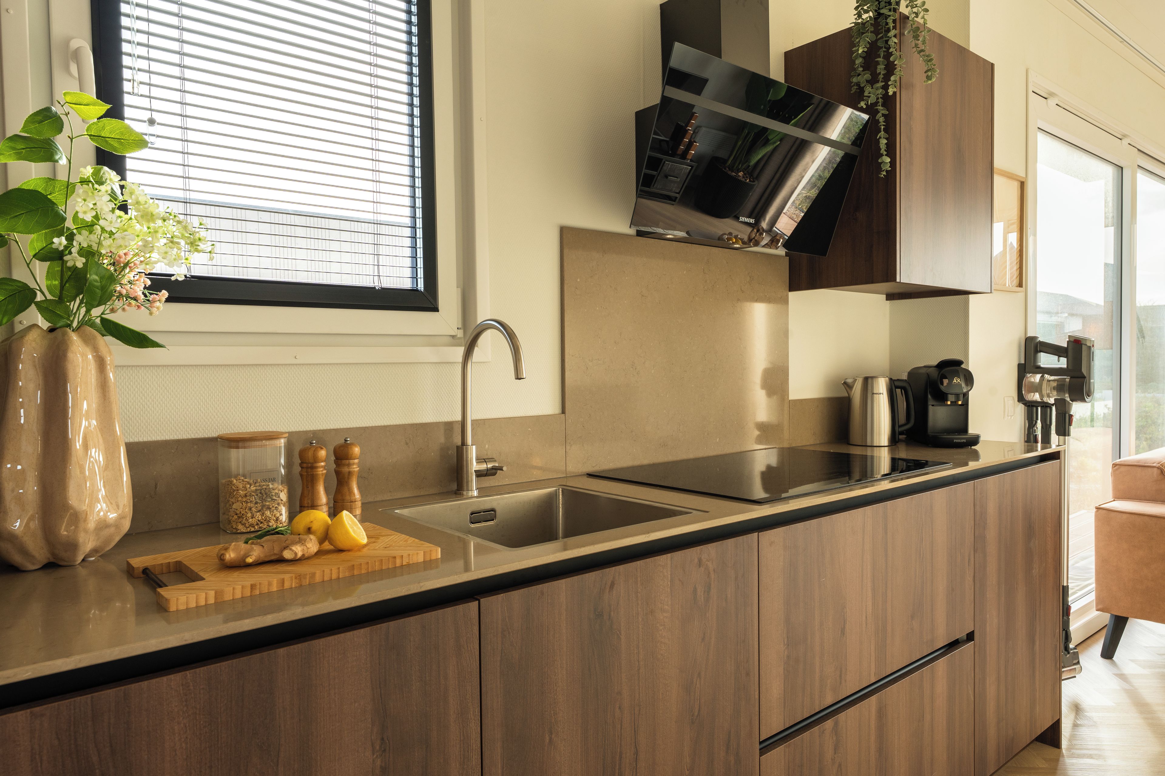 A modern kitchen with a built-in sink, wooden cabinets, a window with blinds, and a potted plant.