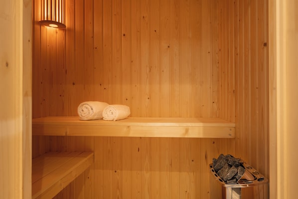 Un sauna de madera con dos toallas enrolladas en un estante y un recipiente metálico con piedras.