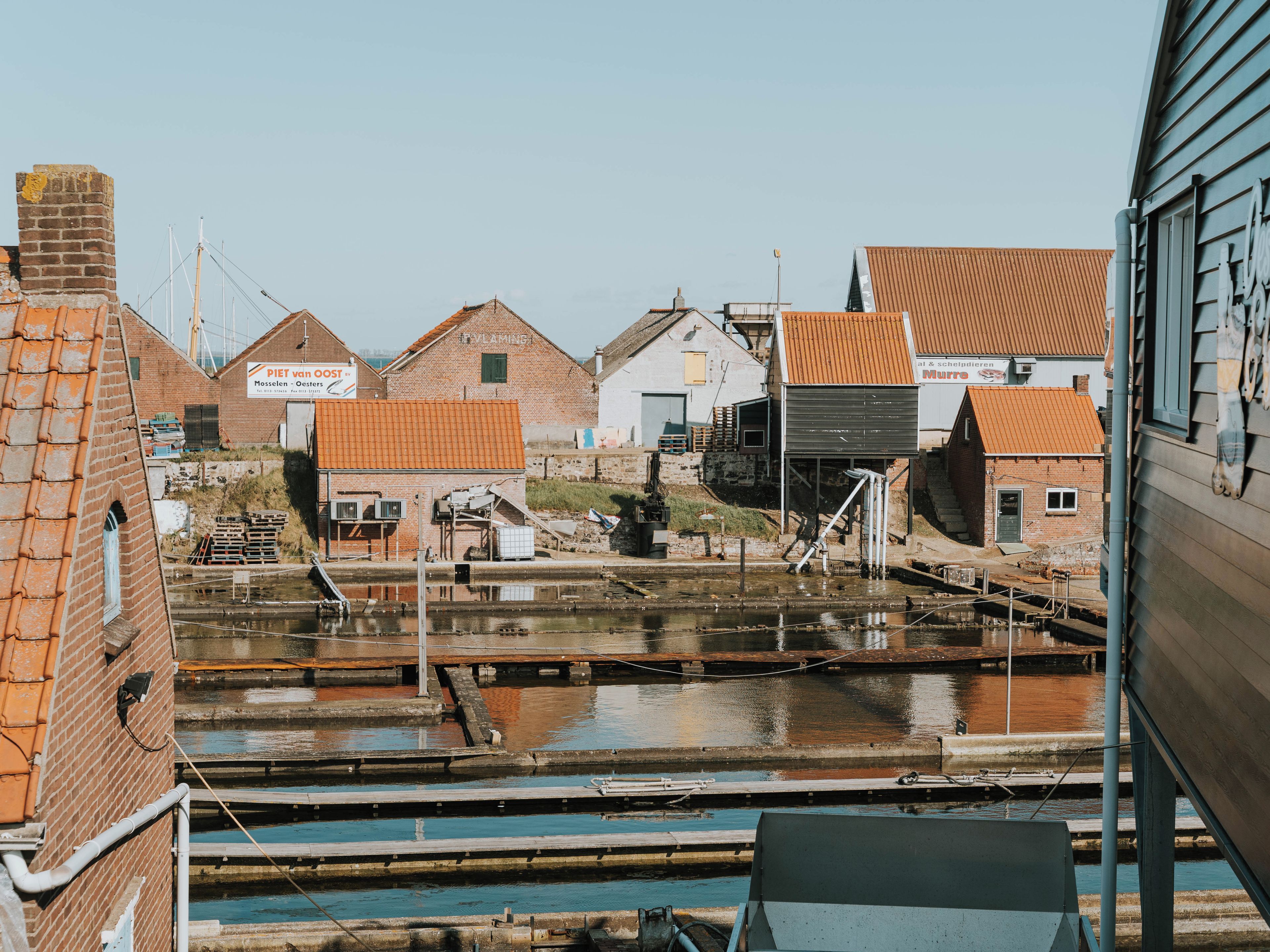 A view of a riverside area with buildings, including a brick structure with a sign that reads 'PIET VAN BOOST.'