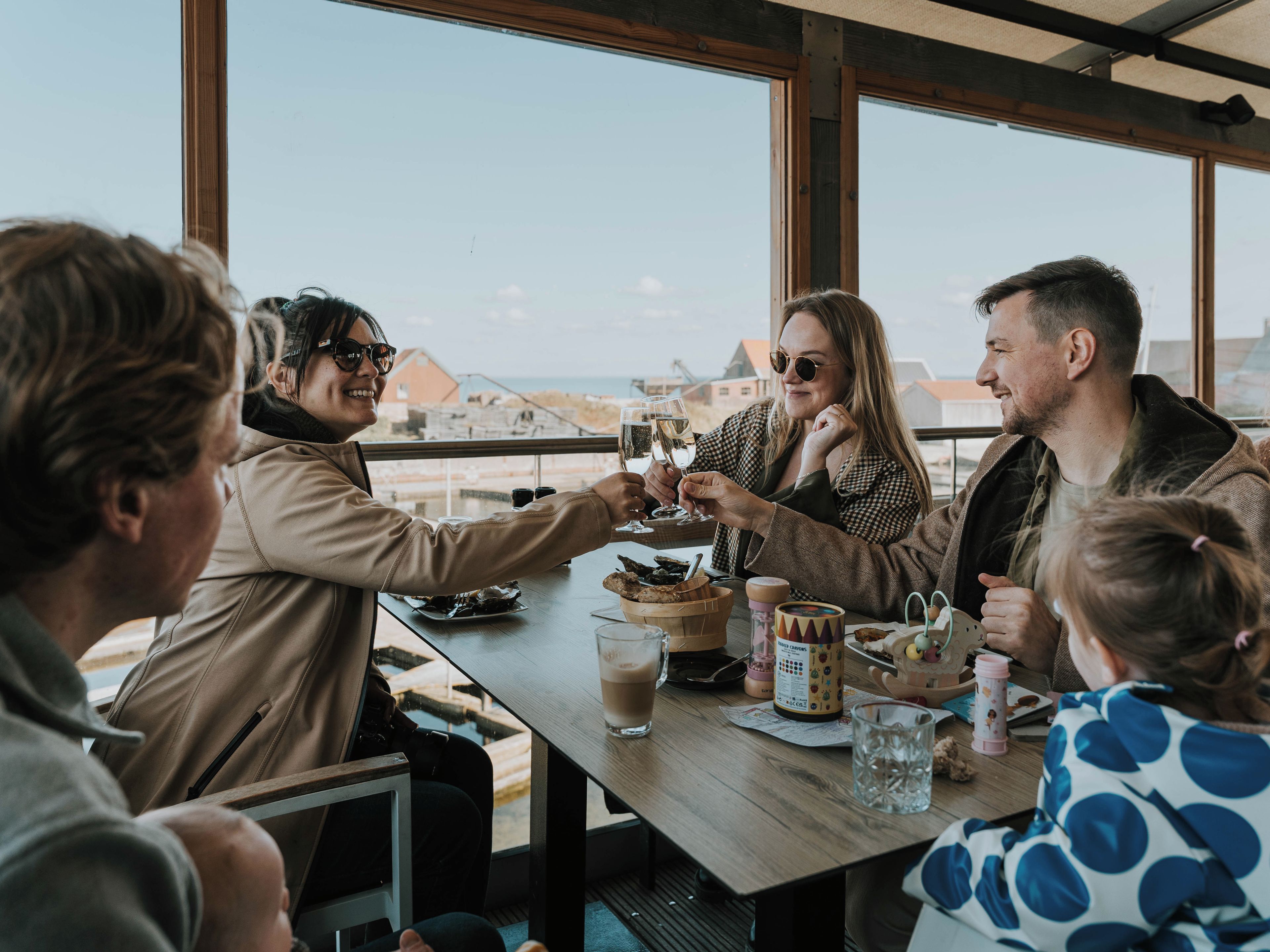 Een groep mensen proost met drankjes aan een tafel met uitzicht op zee.
