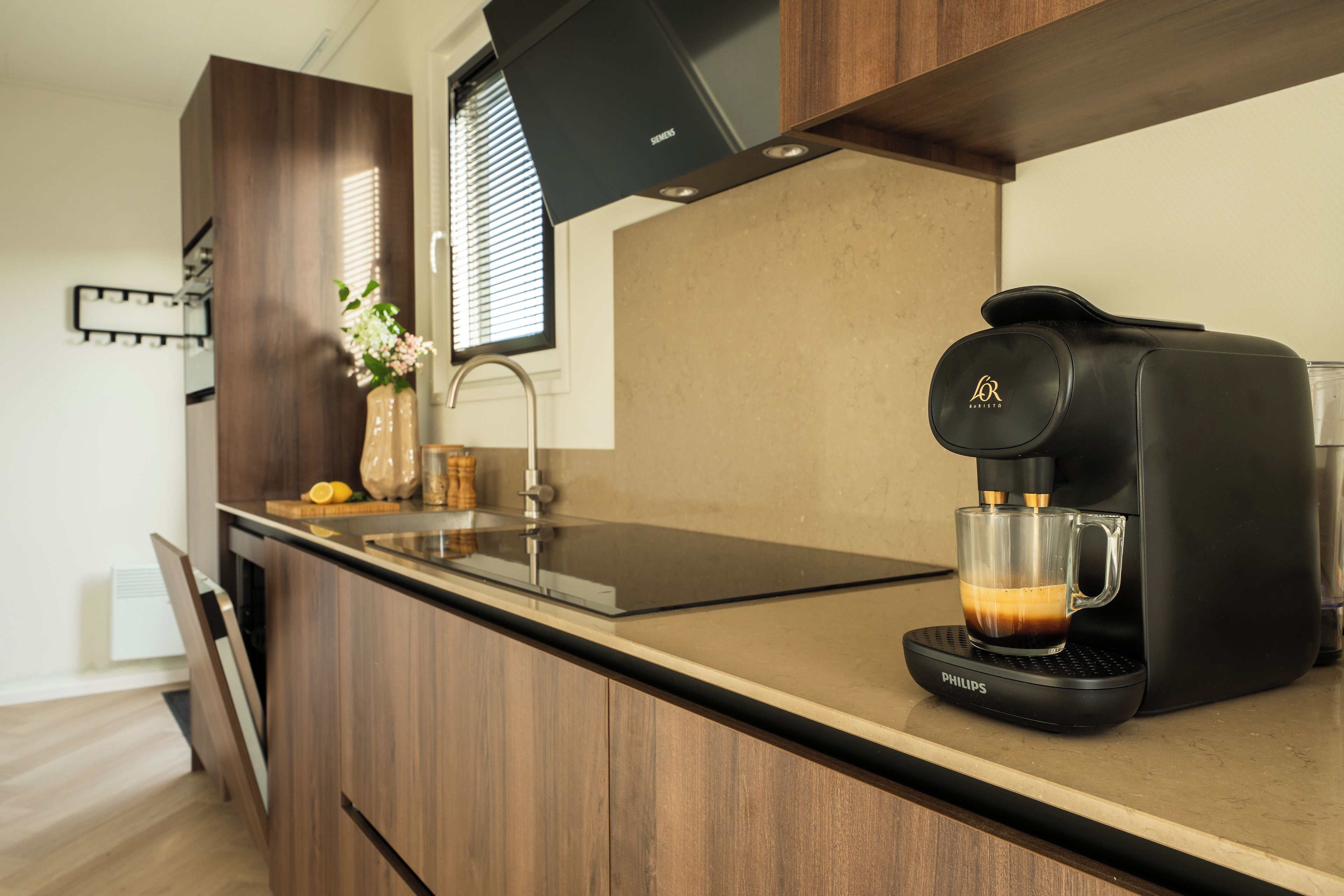 Een moderne keuken met een koffieapparaat, een glazen kop en een vaas met bloemen op het aanrecht.