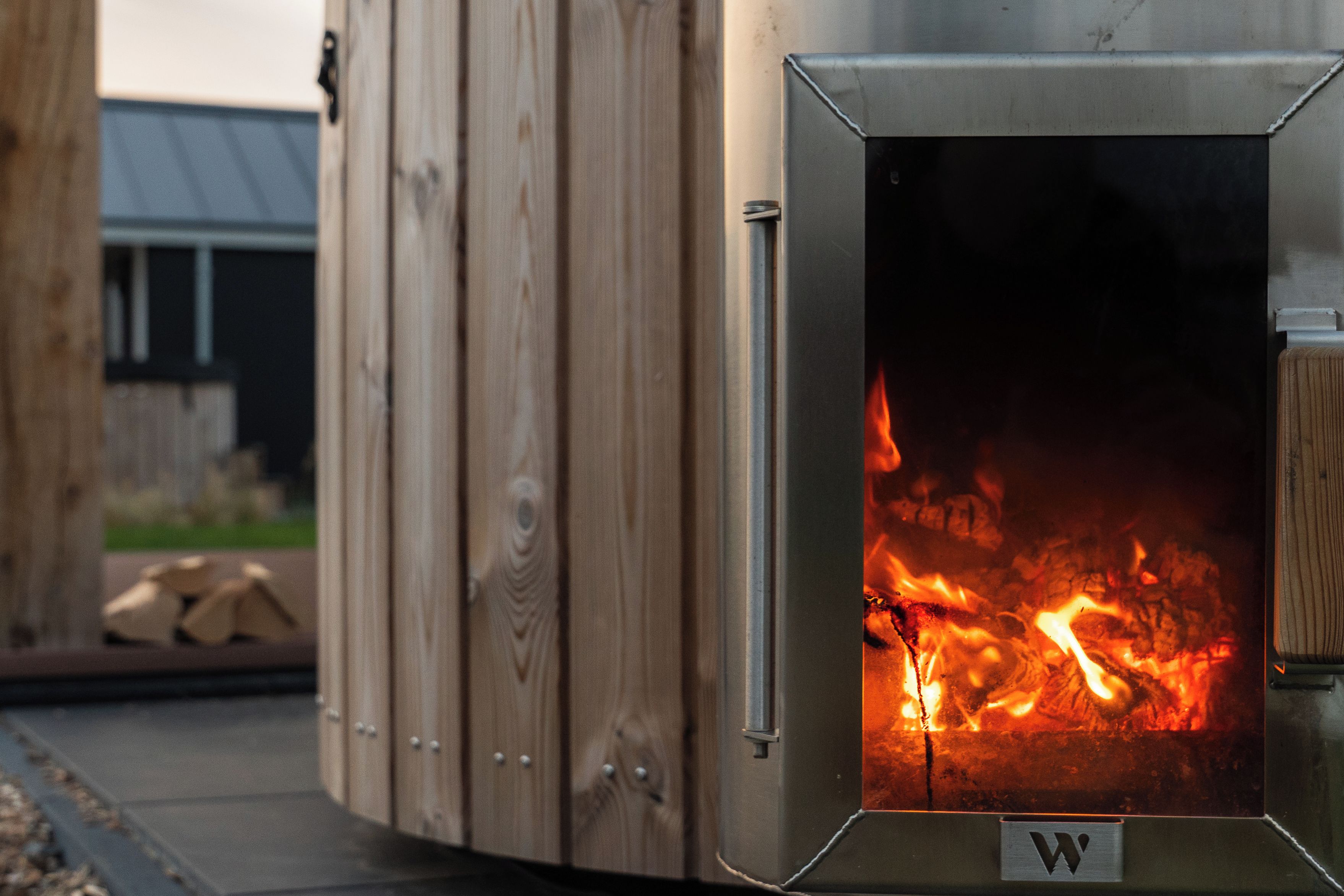 A wood-burning stove with a metal door, set against a wooden backdrop.