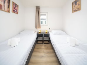 Habitación doble con dos camas, una mesita y una ventana con cortinas.