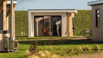 Un bâtiment moderne doté de grandes portes vitrées, d’une terrasse en bois et d’une pelouse à l’avant.