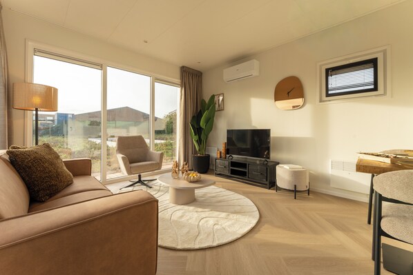 Ein modernes Wohnzimmer mit einer Couch, einem Couchtisch, einem Fernseher und einem großen Fenster mit Blick ins Freie.
