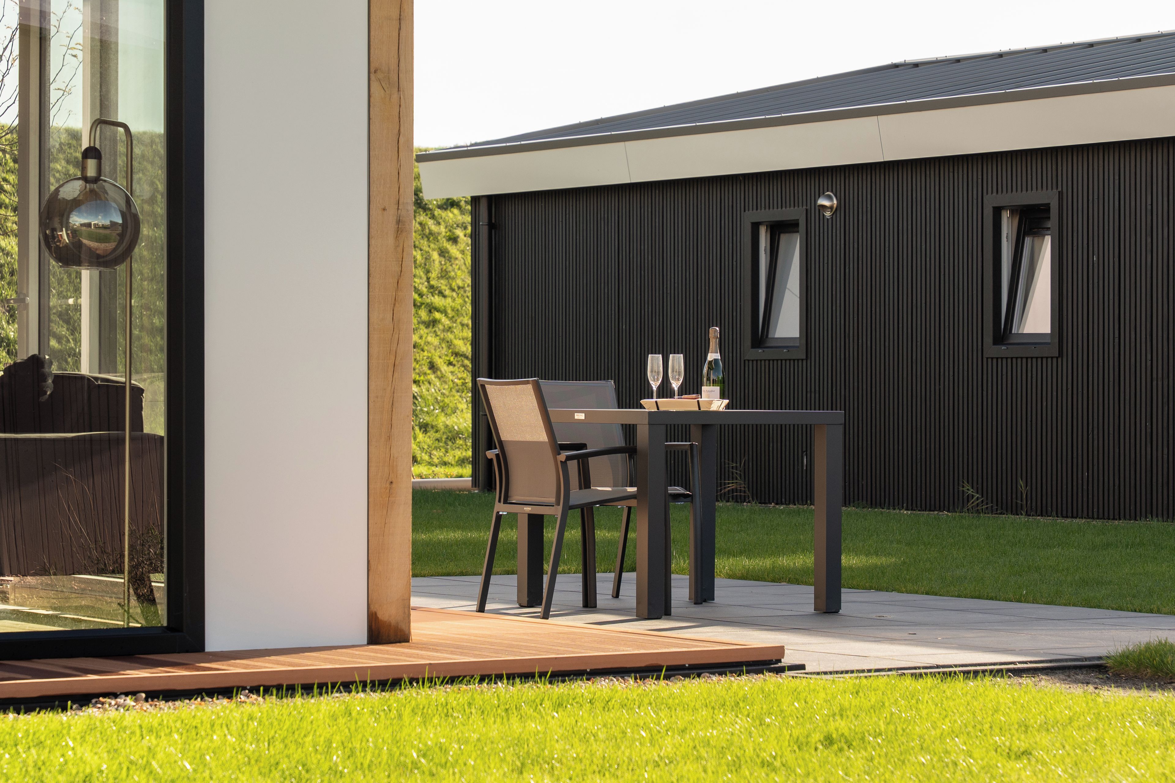 Een modern buitenzitje met een tafel en stoelen, een fles wijn en een glas op de tafel.
