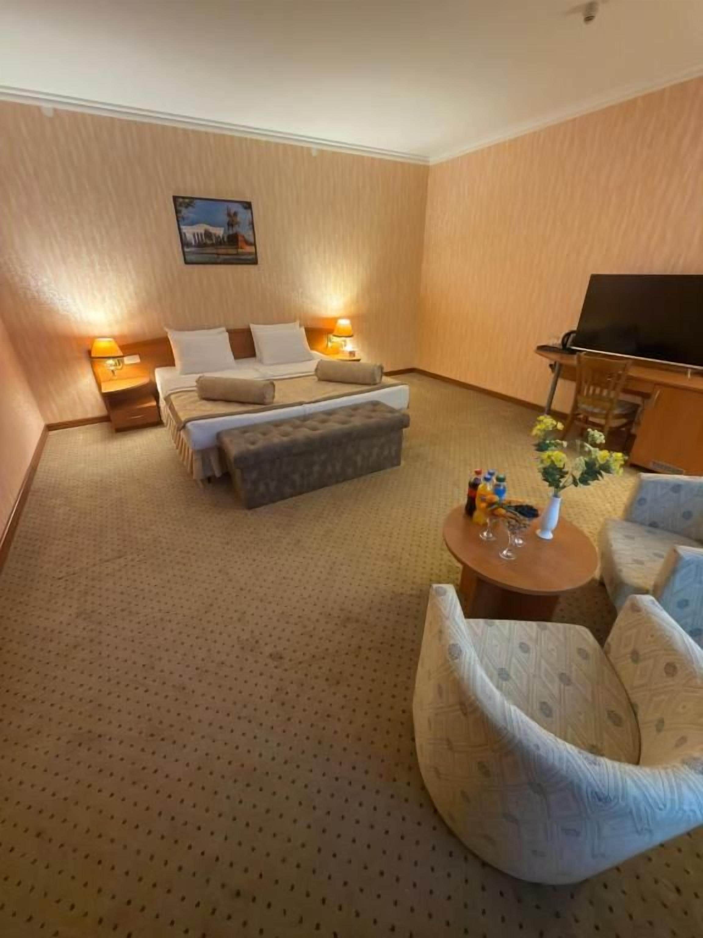 A hotel room with a bed, a sofa, a small table, and a television.