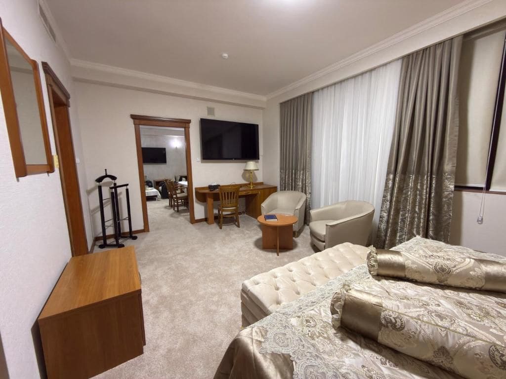 Ein Hotelzimmer mit Bett, Schreibtisch, Stuhl, Fernseher und einem großen Fenster mit Vorhängen.