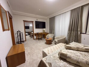 A hotel room with a bed, a desk, a chair, a television, and a large window with curtains.