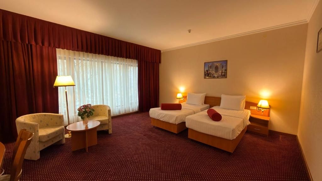 A hotel room with two beds, a sofa, a chair, a small table, and a lamp.