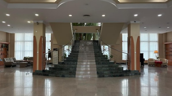 A spacious lobby with a central staircase, seating area, and large windows.