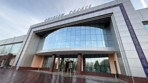 A modern hotel entrance with a glass facade, a nameplate above the doors, and a red carpet leading to the entrance.