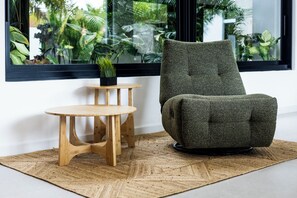Ein modernes Zimmer mit einem mit Grünstoff gepolsterten Sessel, einem Holznachttisch und einer kleinen Topfpflanze.