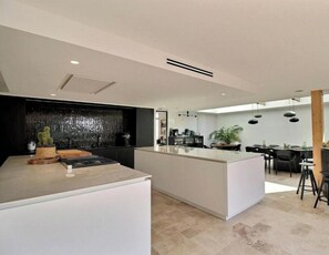 A modern kitchen with a central island, a dining area with a table and chairs, and a kitchen counter with appliances. - Villa with suites and spa in La Trinité-sur-Mer (LA TRINITE-SUR-MER)