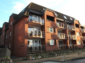A multi-story residential building with balconies, brick exterior, and a stone foundation. - Atrium Holiday Apartment 33 (Sylt)