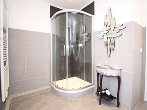A corner bathroom with a glass-enclosed shower, a vanity with a mirror, and a radiator. - Atrium Holiday Apartment 33 (Sylt)