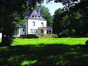 A two-story house with a balcony, surrounded by a well-maintained lawn and trees. - Holiday Apartment With 1 Bedroom (Lambrecht)