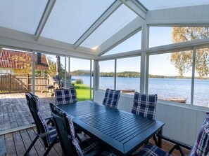 A covered outdoor seating area with a table and chairs, overlooking a lake. - Holiday Home With 3 Bedrooms (Ambjörnarp)