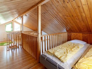 A room with a sloped ceiling, wooden flooring, a bed with a mattress and pillows, a window, and a small balcony area. - Holiday Home With 3 Bedrooms (Ambjörnarp)