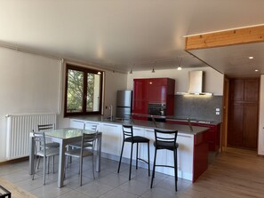 Une cuisine moderne dotée d’un îlot central, de deux tabourets de bar, d’une table à manger avec des chaises et d’une fenêtre qui laisse entrer la lumière naturelle.