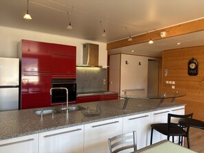 A modern kitchen with a red refrigerator, stainless steel appliances, granite countertops, and a glass dining table. - Apartment with balcony and ski slopes view (Les Deux Alpes)