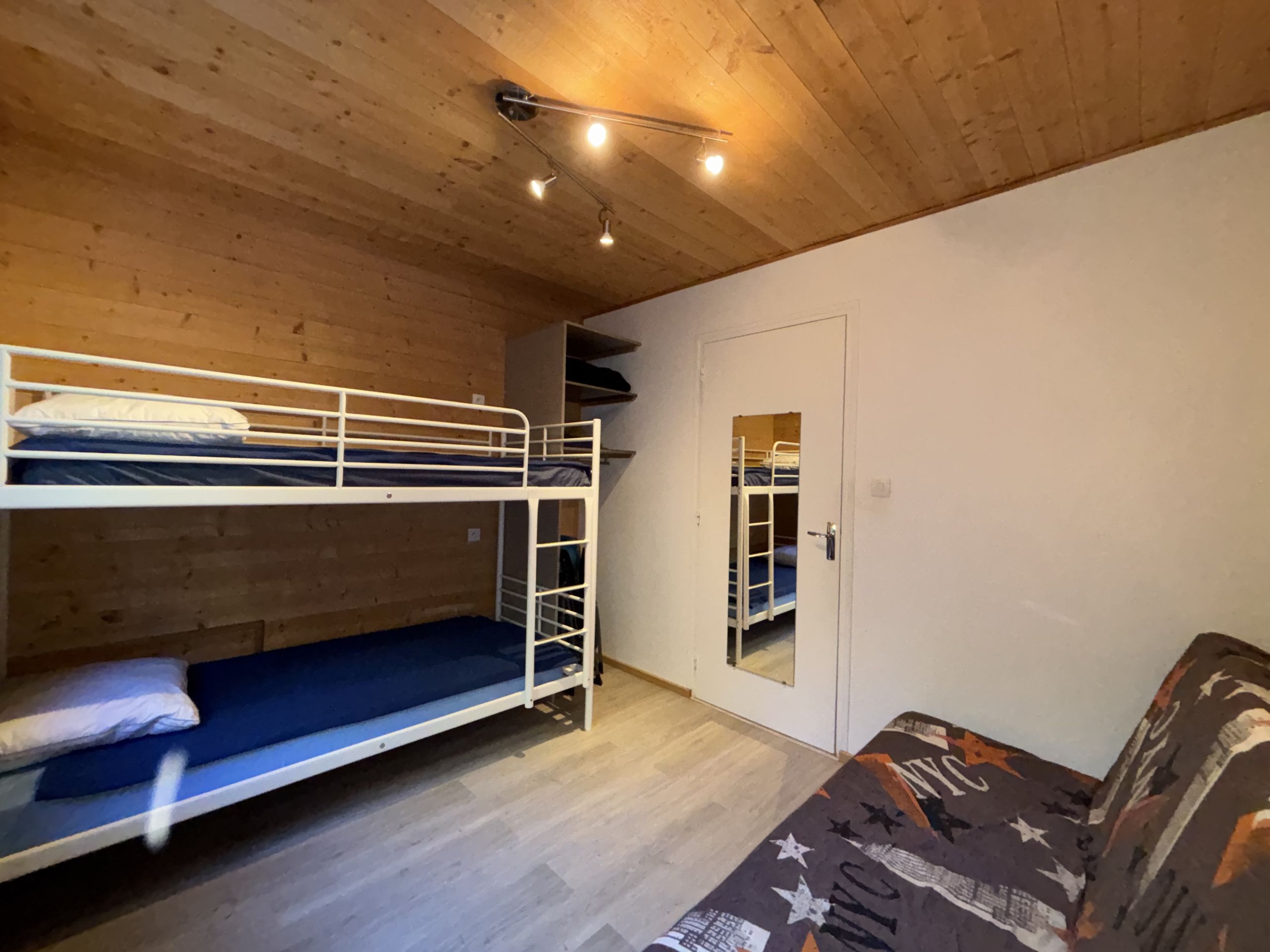 Une chambre avec un lit superposé, une porte, une petite fenêtre et un canapé à motifs.