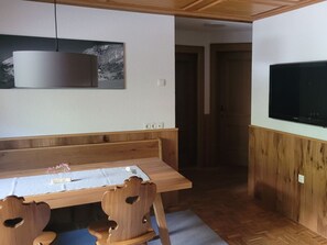 A room with a wooden dining table, chairs, a television, and a wall-mounted picture. - Holiday Apartment With 1 Bedroom (Schoppernau)