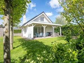 A single-story house with a covered patio, a fenced yard, and a tree in the foreground. - Holiday Home in Renesse With Swimming Pool (Renesse)
