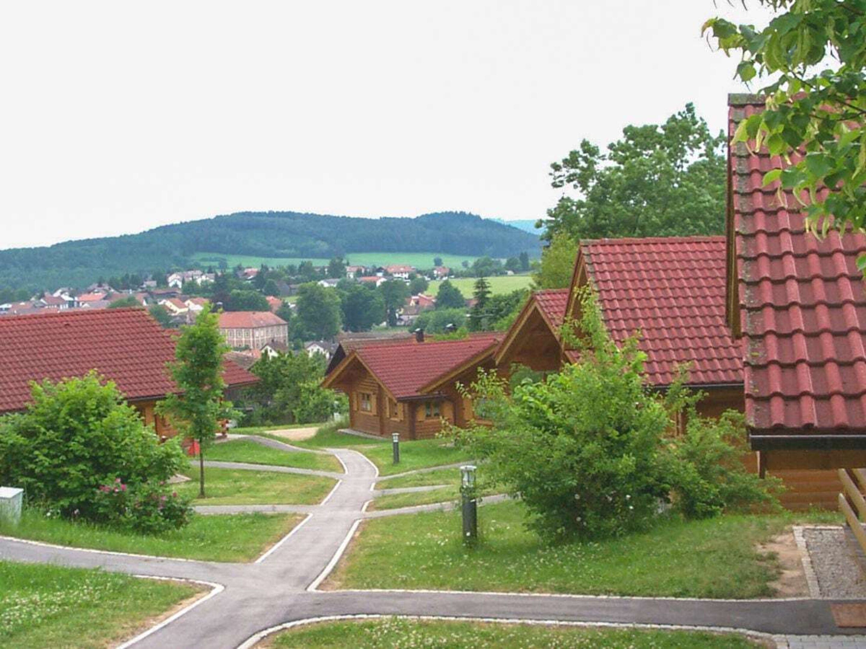 A rural village with traditional red-tiled roofs, a winding road, and a view of the surrounding hills.