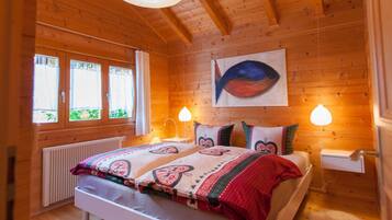 A wooden-paneled room with a bed, two bedside lamps, a radiator, and a window with curtains.
