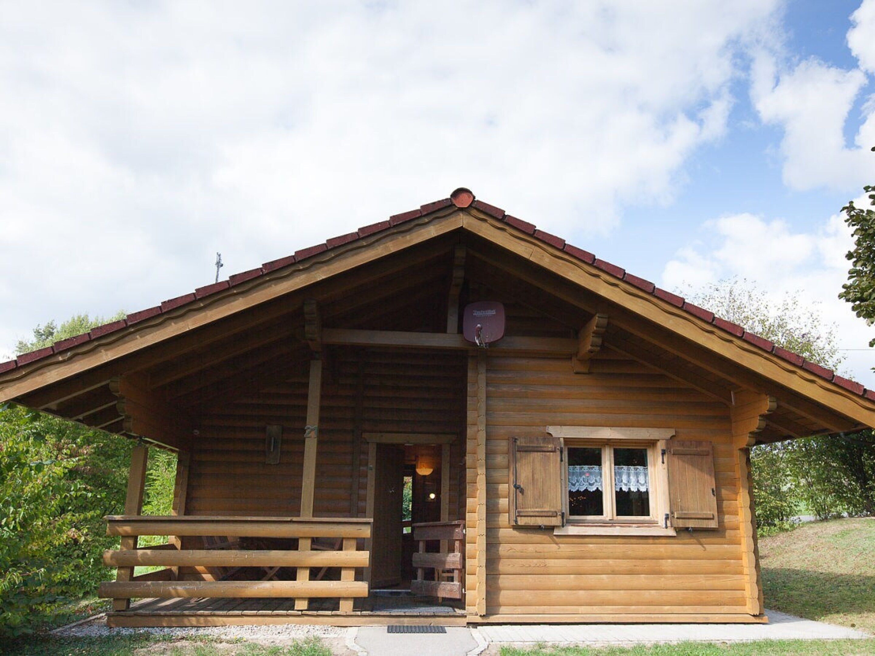 A wooden cabin with a pitched roof, a porch with benches, and a small window with shutters.
