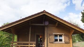 A wooden cabin with a pitched roof, a porch with benches, and a small window with shutters.