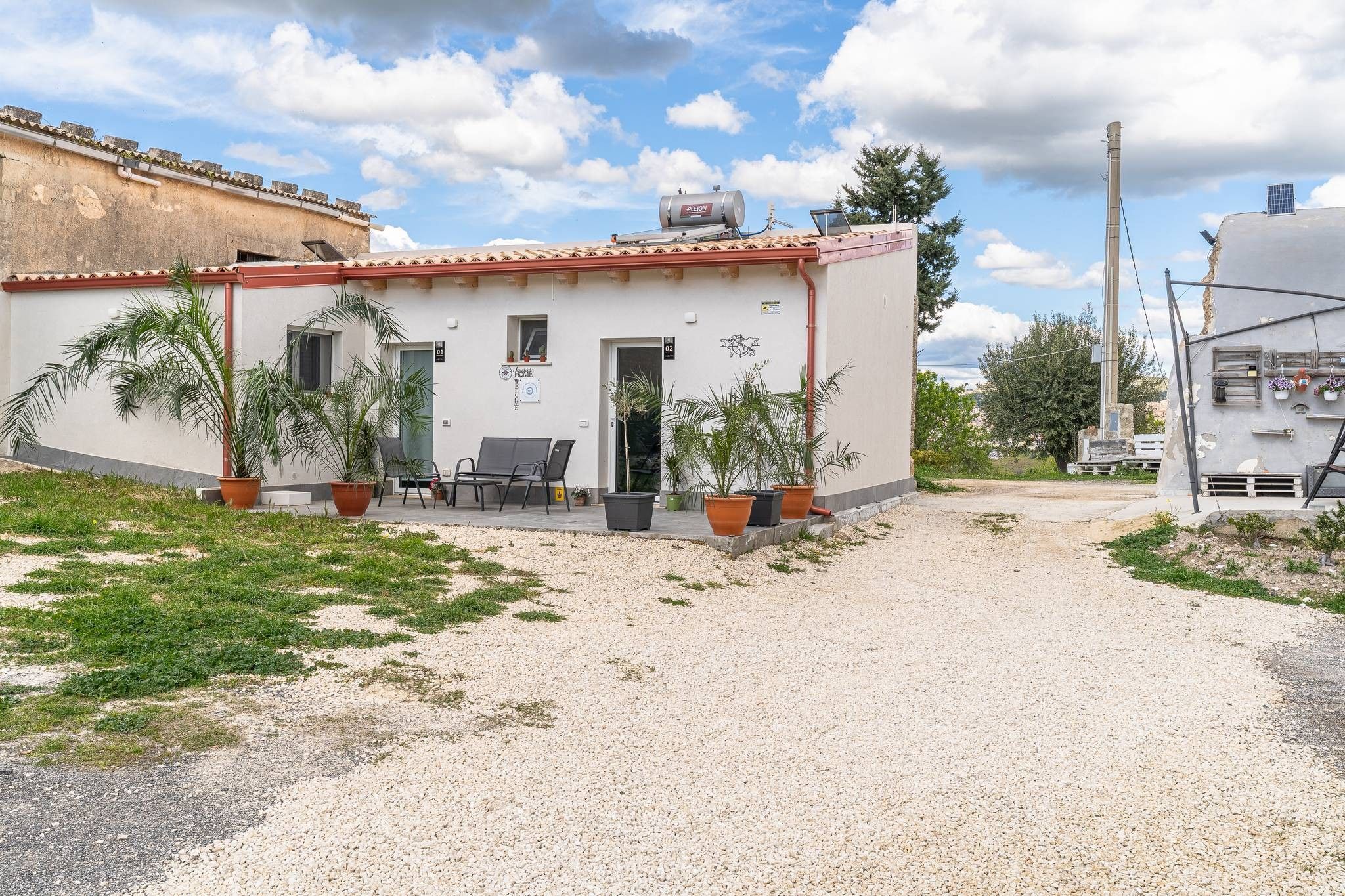 A building with a gravel driveway, potted plants, and outdoor seating.