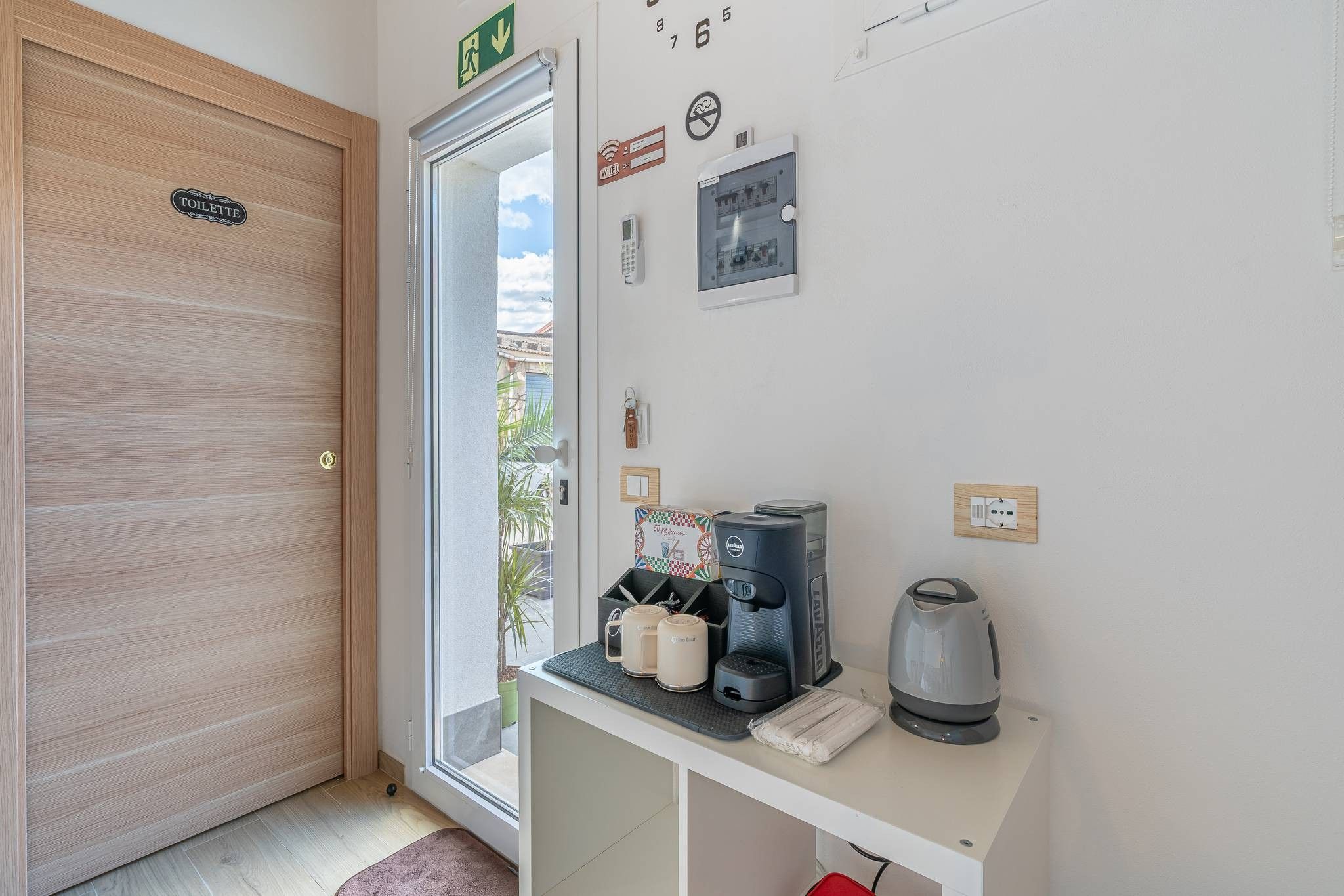 Ein Hotelzimmer mit Holztür, einem kleinen Tisch mit Kaffeemaschine, Tassen und einem Wasserkocher.