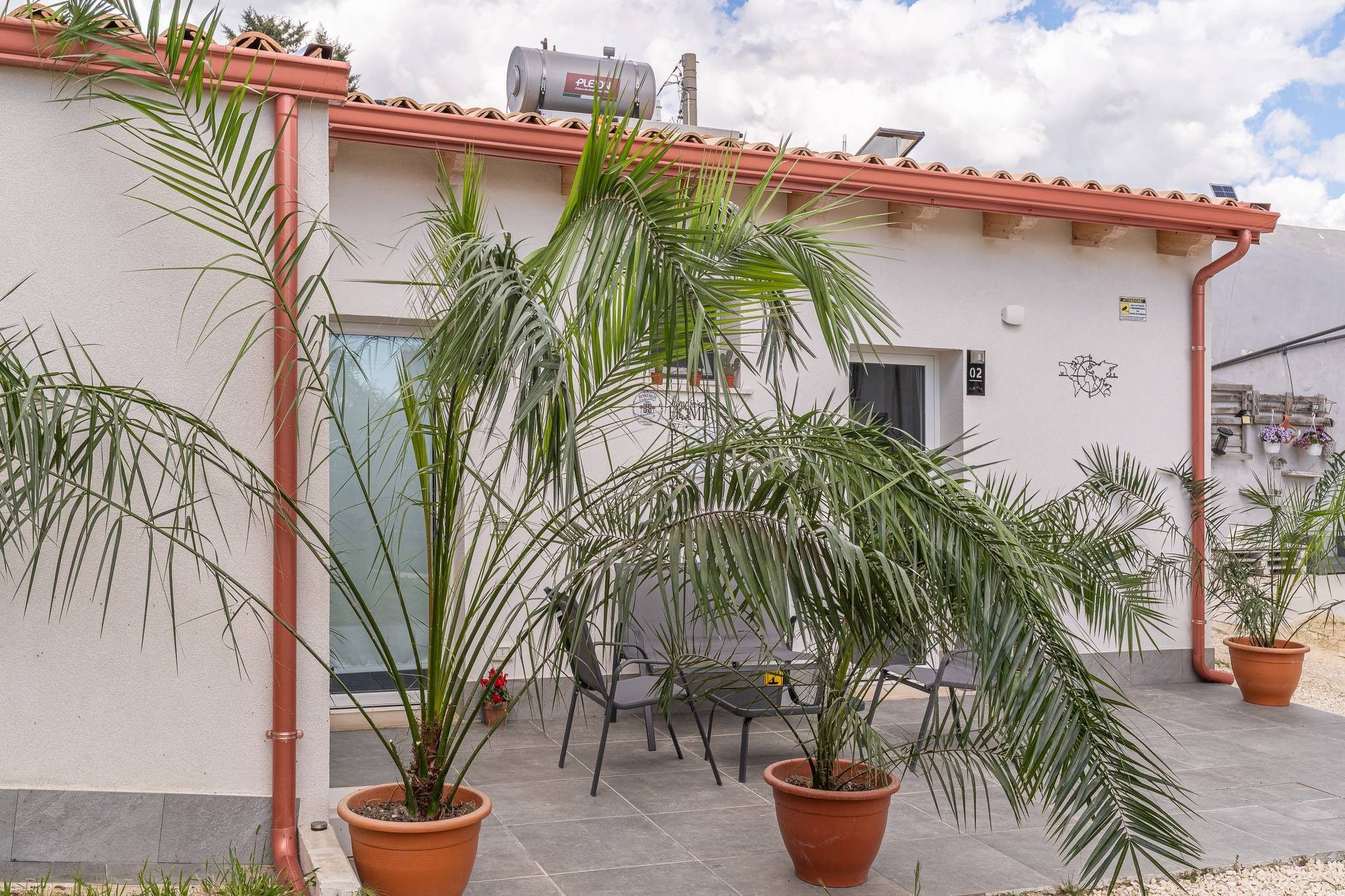 En bygning med tegltag, plantekasser og en terrasse med stole og et bord.