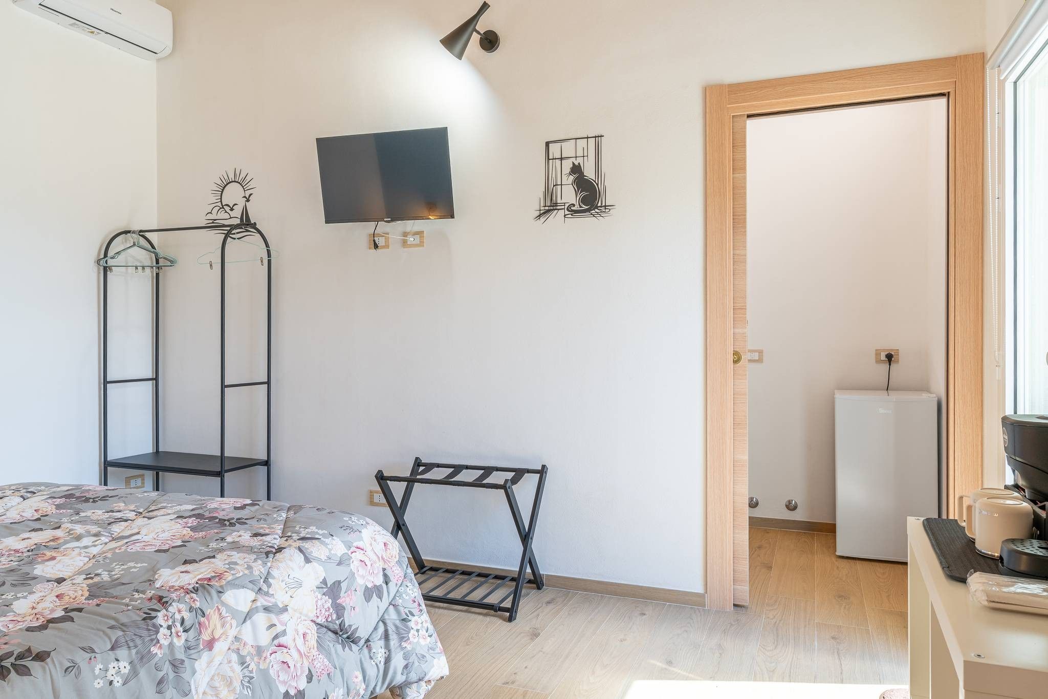 Une chambre à coucher comprenant un lit, un téléviseur, un porte-manteau et une porte donnant sur une autre pièce.