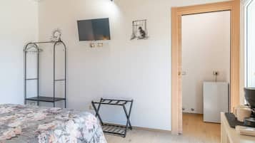Une chambre à coucher comprenant un lit, un téléviseur, un porte-manteau et une porte donnant sur une autre pièce.