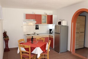 A compact kitchen with a dining table, chairs, and basic appliances. - A5 - Comfortable apartment with terrace, garden and sea view (Barbat na Rabu)
