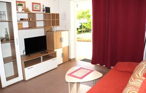 A living room with a TV, wooden shelves, a small table, and a red curtain. - A5 - Comfortable apartment with terrace, garden and sea view (Barbat na Rabu)